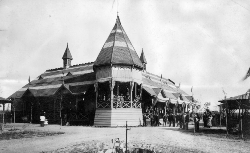 Sans Souci concert gardens.Members of a band pose on a gazebo-like bandstand attached to a building at the concert gardens in San Souci Park in the Washington Park West neighborhood of Denver, Colorado. Men and women stand on the porch and on the ground nearby. The building features a high pitched roof, wrap-around porches, awnings, and small ornamental steeples. Courtesy DPL Western History Collection X-27716