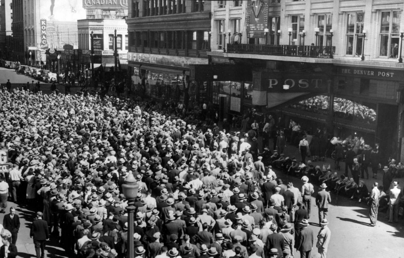 Whatta Game! People crowd Champa Street by the Denver Post newspaper headquarters in downtown Denver, Colorado, to listen to a baseball game. An electric scoreboard is above storefronts on a balcony on the Denver Post building; canopy reads: "Post." Business signs read: "Komac" and "Canadian Club." Title from newspaper clipping attached to back of photoprint; also reads: "Just a portion of the huge crowd that gathered in front of The Post Wednesday and thrilled, pitch by pitch, to the Cub's victory over the Tigers in the opening game of the World Series. Thursday, and all remaining days of the series, these games will be played for you on The Post scoreboard." 1935 October 3. Courtesy DPL Western History CollectionX-28817