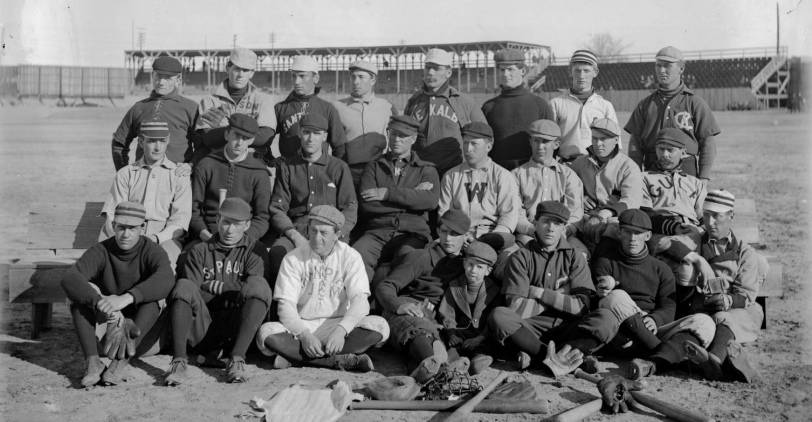 Members of the Denver Bears baseball team pose outdoors at a baseball field in Denver, Colorado. They are identified as: standing: Len "Dad" Shirk, Walter Price (P) Walter Bissell, unknown, "Old Hoss" Hausen (C), Happy "Klondike" Kane (P), J. H. Vizard (OF), Jack Holland (INF & OF). Middle: Pop Eyler (P), Dakin "Dusty" Miller (OF), Tom "Tacks" Parrott (P, OF, INF), Charley Kight (P) Charles "Princeton Charlie" Reilly (3B), Charlie Zeitz (OF), W. E. "Bill" Hickey (INF), Al Hickey (C). Front: Mons "Eddie" Webster (P), Walter "Wizard" Preston (CF), Jack Sullivan, Pearl "Casey" Barnes (INF), Clarence Leisenring, Mascot, Joe Tinker (2B), and W. E. Hurry McNeeley (P & INF). Courtesy History Colorado Collection CHS-B1427