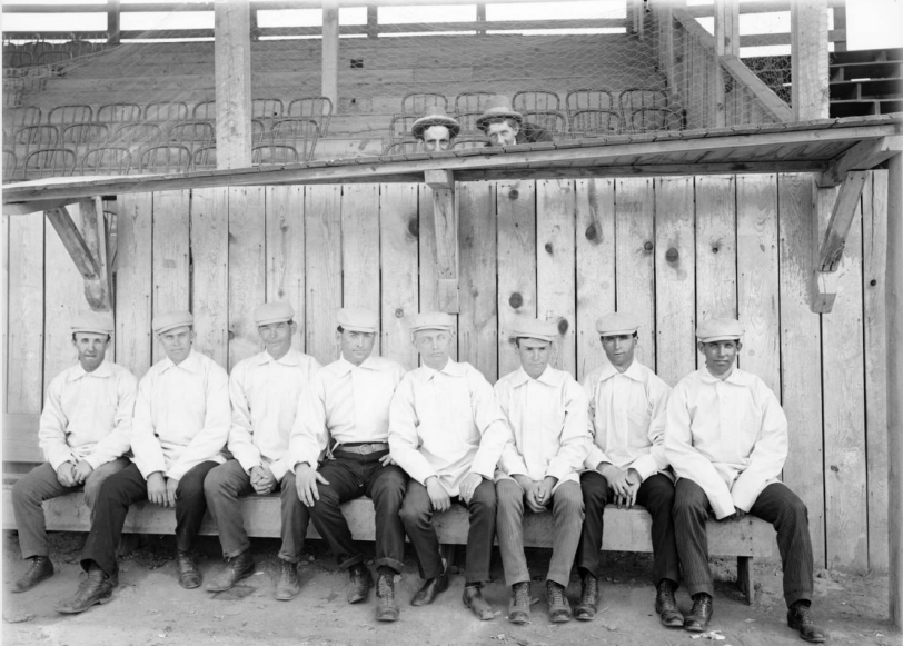 Members of the Denver Bears baseball team pose in a dugout in Broadway Park at 6th (Sixth) Avenue and Broadway in Denver, Colorado. They are identified as (left to right): Earnest "Kid" Mohler (2B), W. A. "Bill" Hickey (IF & OF), Jack Holland (IF & OF), Joe Tinker (IF), Eddie "Kid" Lewee (SS), Charlie Zeitz (OF), Henry Schmidt (P), and unknown. [1900] Courtesy History Colorado Collection CHS-B1456
